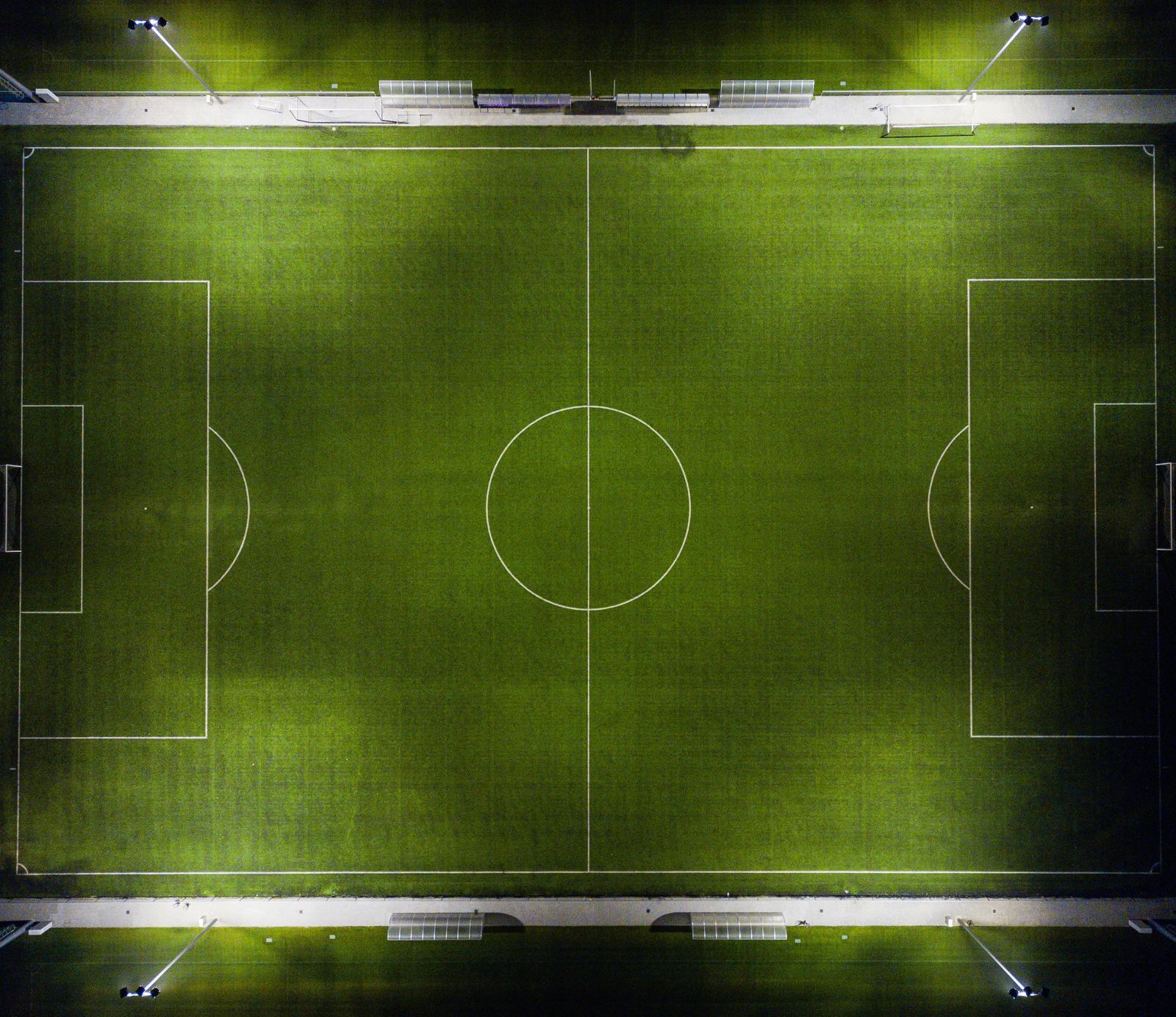 A floodlit football pitch from above, with the P2P Academy crest